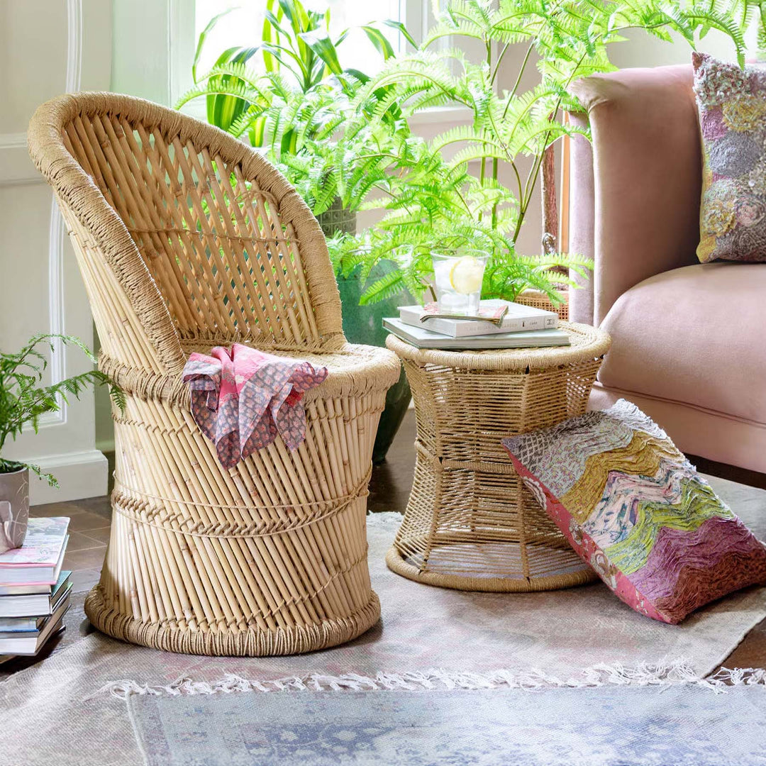 Vintage boho décor featuring rattan chair and table, colorful cushions, and lush plants creating an eclectic and warm home atmosphere.