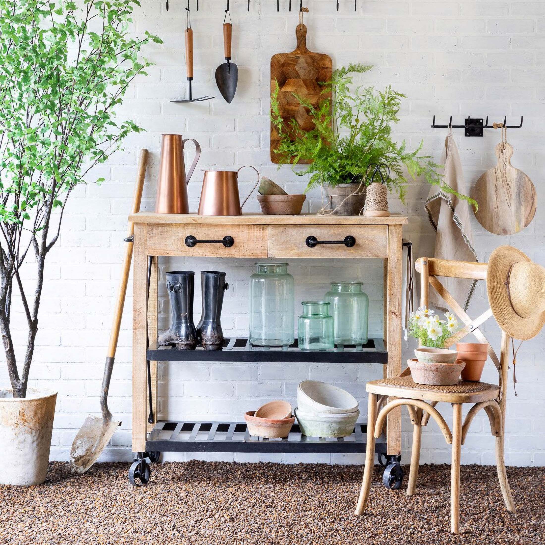 Rustic garden setup with wooden table, vintage accents, plants, pots, and garden tools, evoking an antique outdoor décor ambiance.