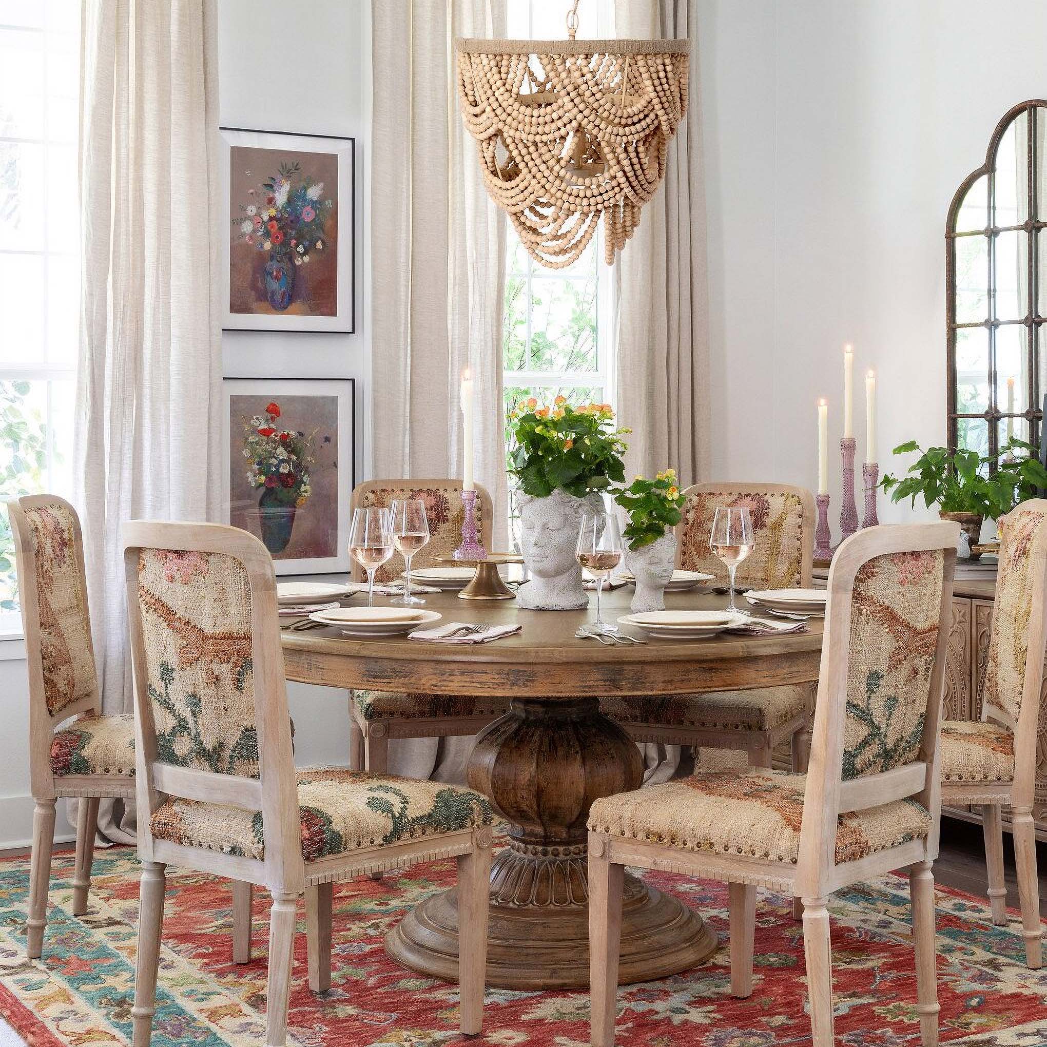 Vintage-style dining room with ornate chairs, rustic wooden table, floral rug, and a beaded chandelier for classic home decor elegance.