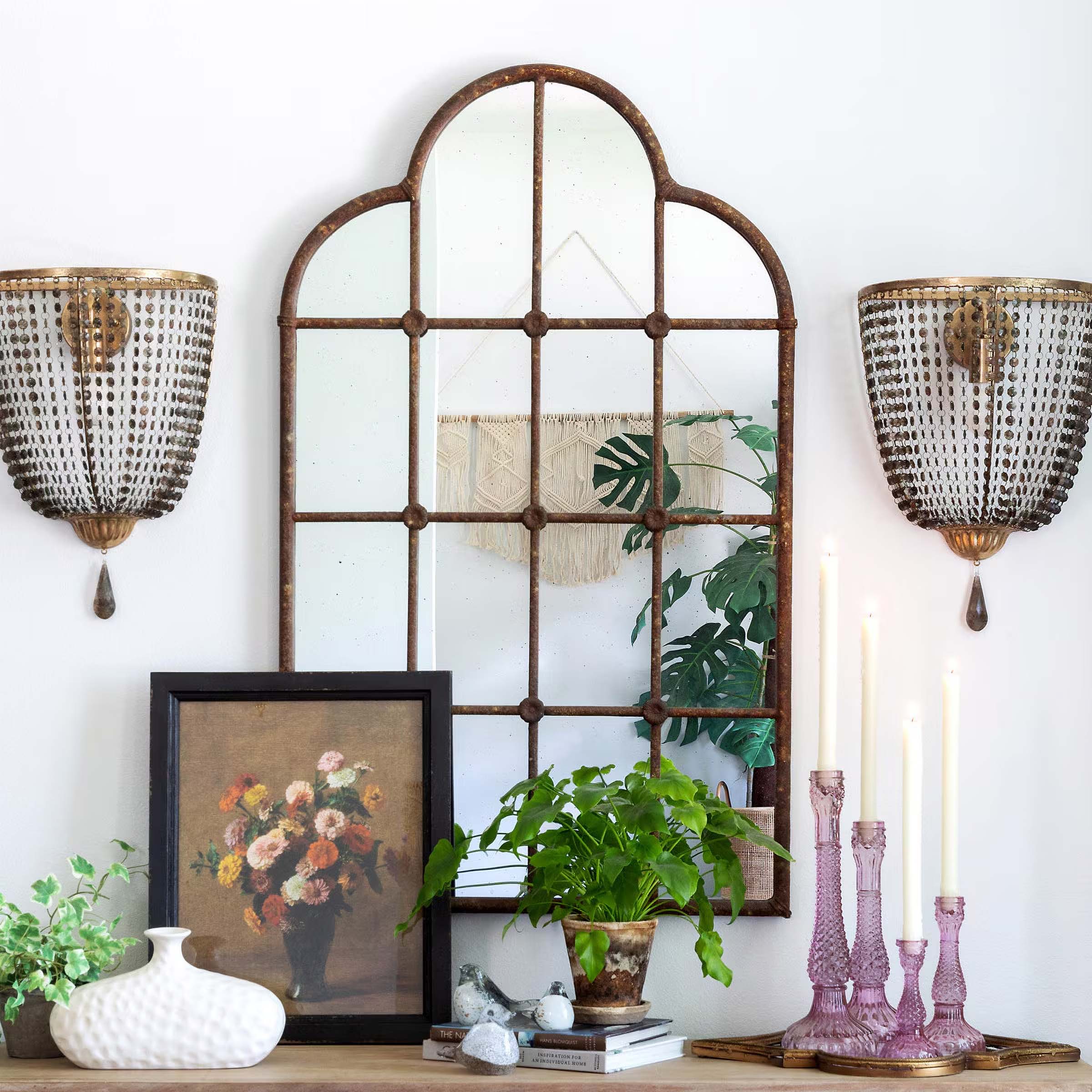 Vintage-inspired arched mirror with elegant sconces, floral artwork, and decor, adding charm and depth to a modern living space.