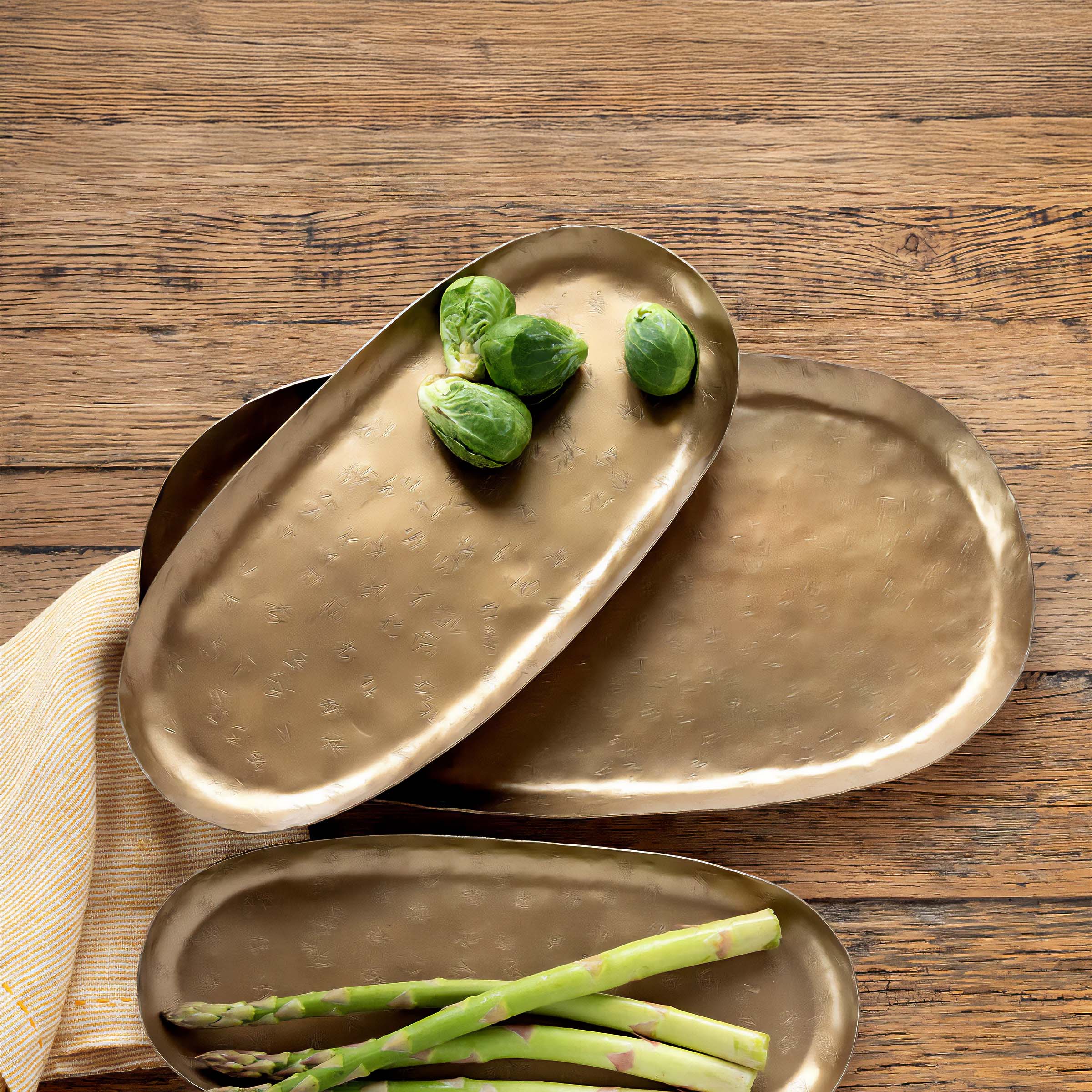 Vintage brass serving trays with vegetables on rustic wooden table, perfect for entertaining and hospitality.