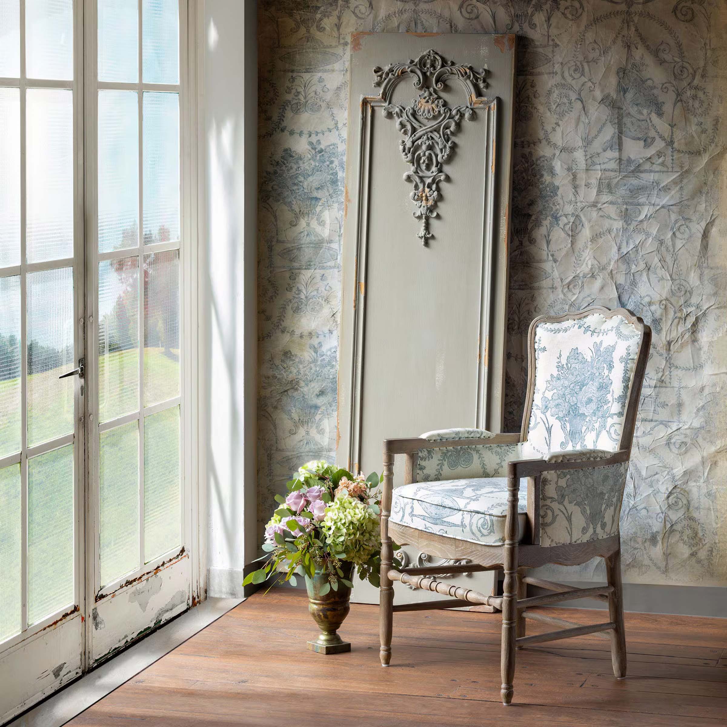 Vintage-style décor with ornate chair, floral vase, and decorative panel by sunlit window. Ideal for antique charm in home design.