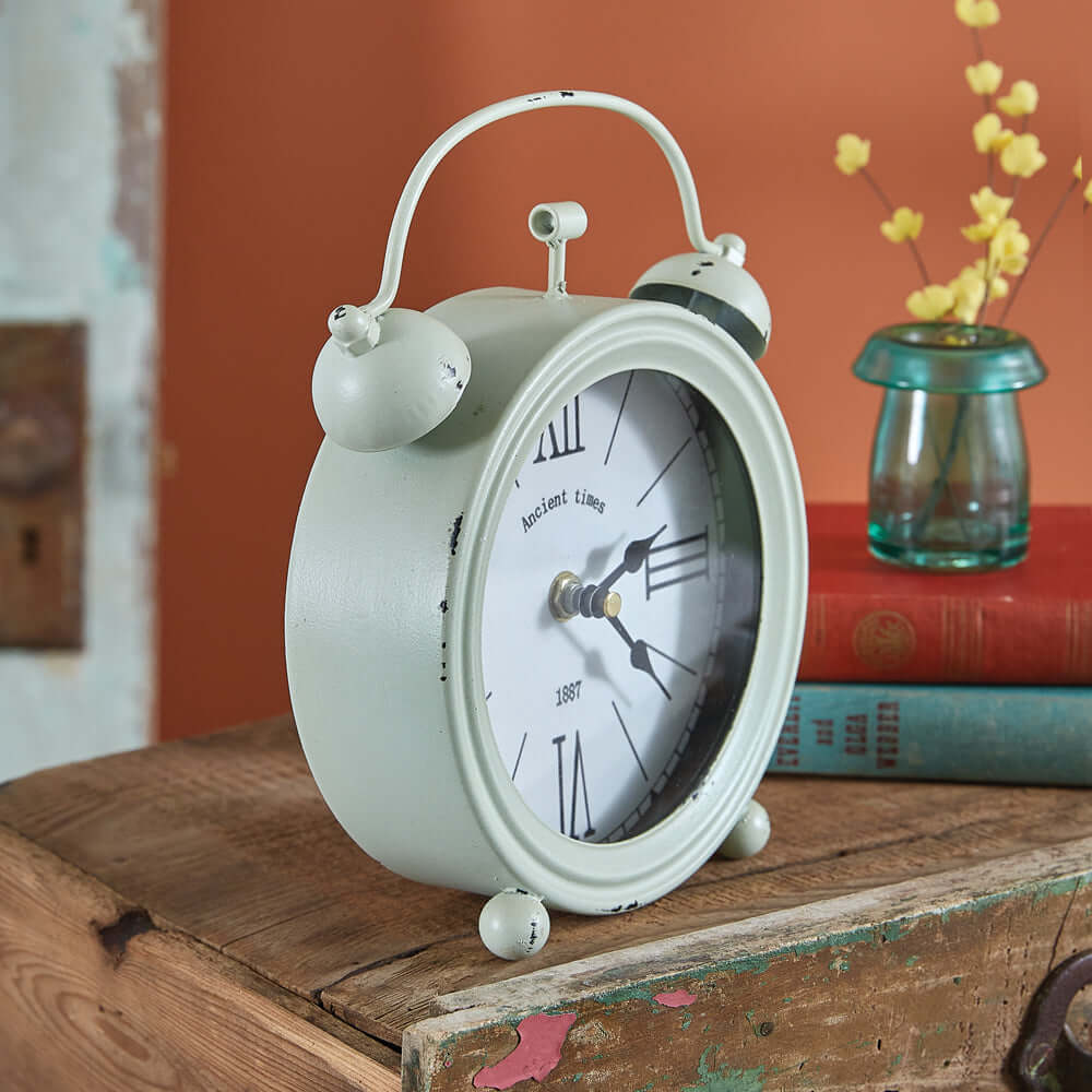 Vintage mint green twin bell alarm clock with distressed edges on a rustic wooden table, featuring Roman numerals and nostalgic charm.