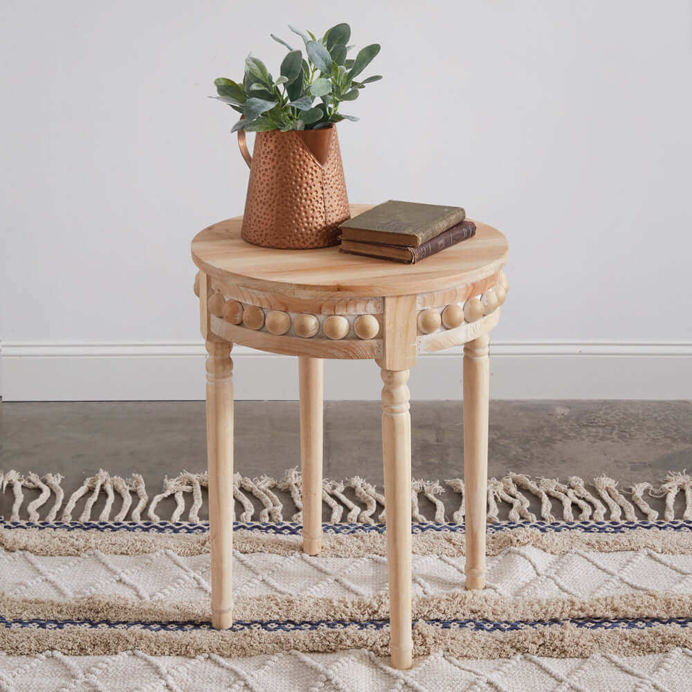 Round Boho side table with natural wood finish, decorative beads, and a plant, enhancing cozy, eclectic decor.