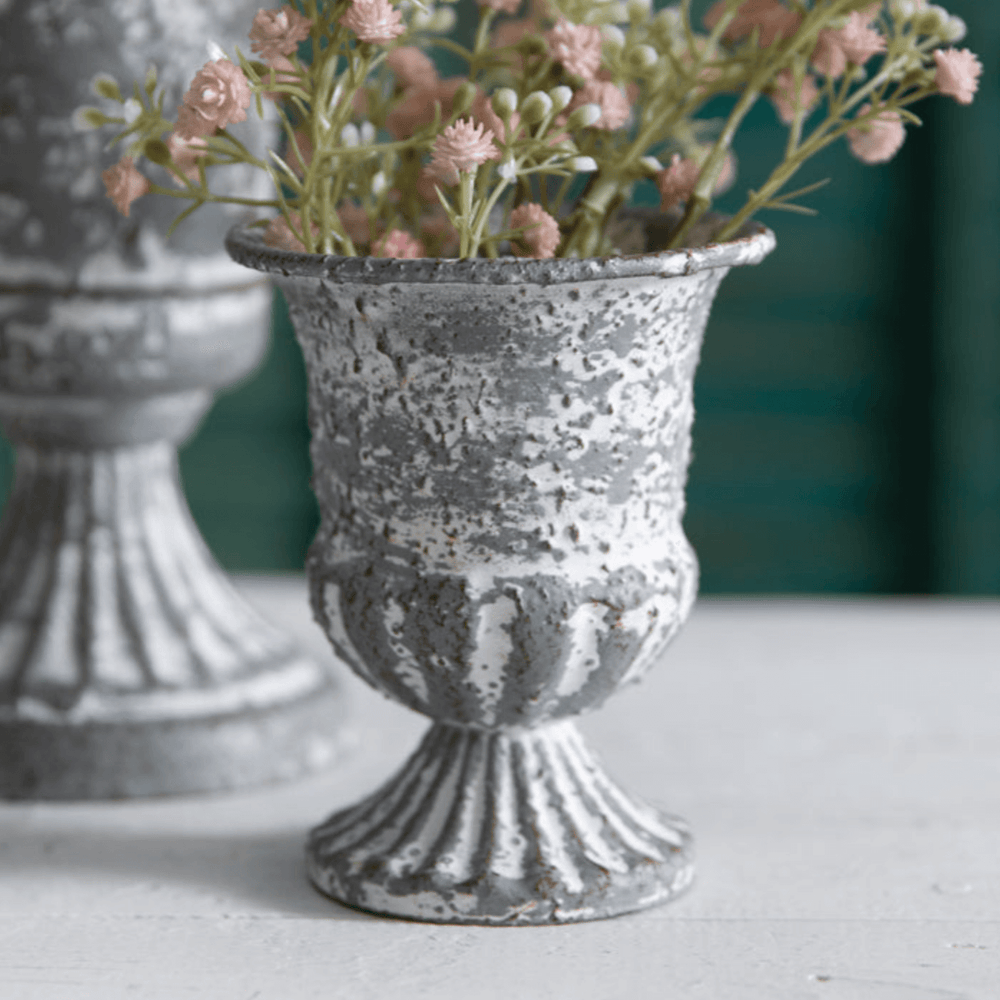 Antique farmhouse metal urn with distressed finish, vintage charm and flowers, perfect for rustic home decor.