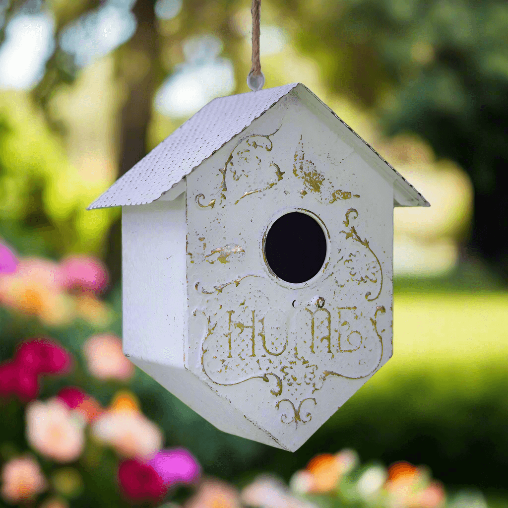 Cottagecore garden birdhouse with embossed filigree, faded white finish, and hanging design surrounded by colorful flowers.
