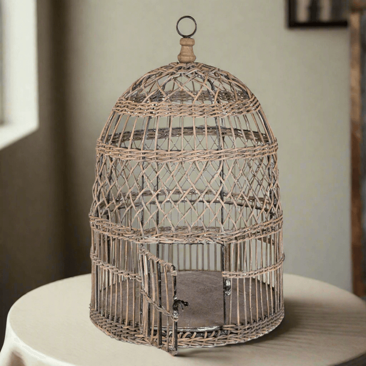 Vintage wicker and metal bird cage on table; handcrafted blend of intricate design and sturdy materials, evoking nostalgic charm.