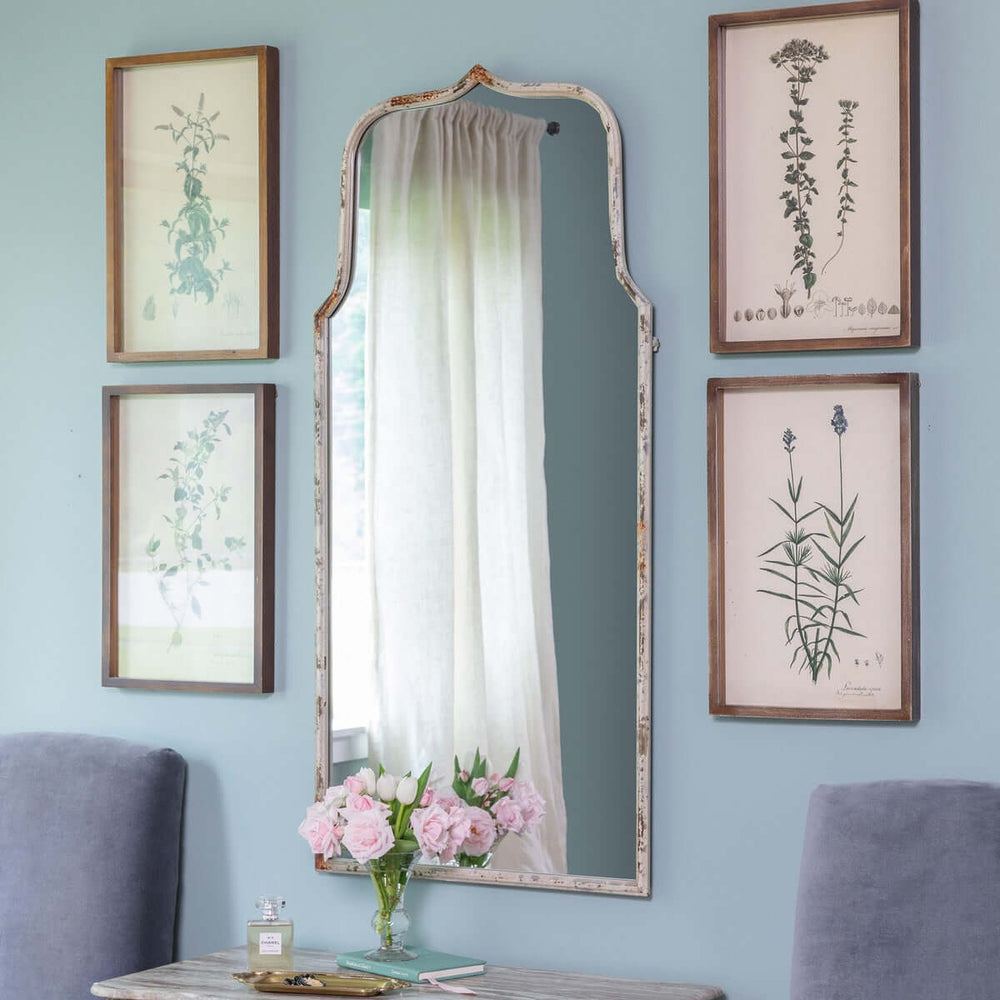 French Country arch mirror with distressed white frame in a vintage-inspired room with botanical prints and soft decor.