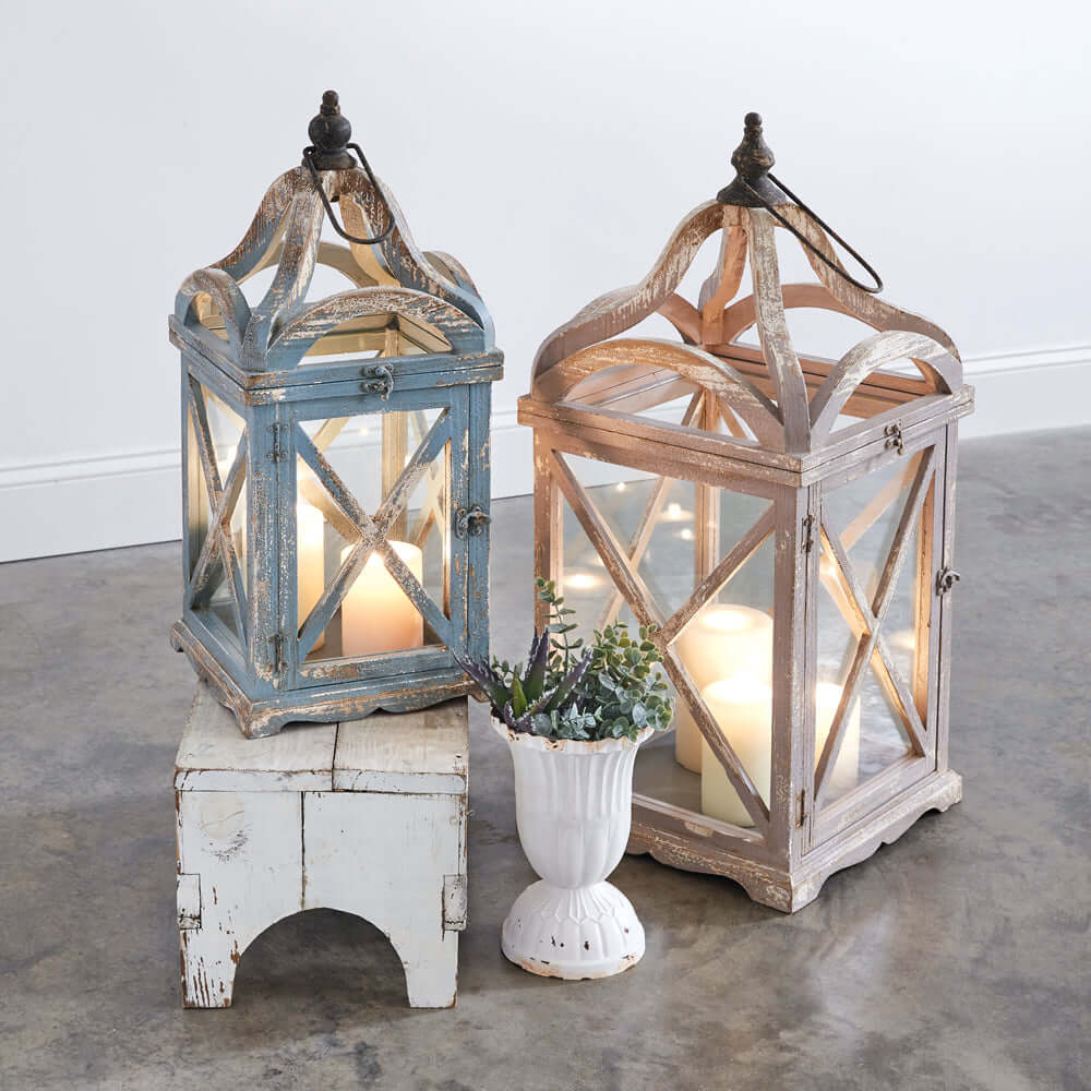 Set of 2 French Country lanterns with arched tops in blue and pink distressed finish, glowing candles inside.