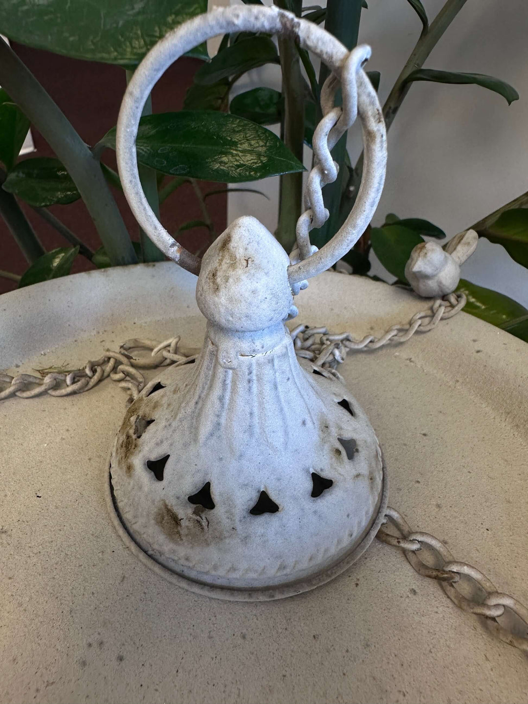 Vintage distressed white hanging bird feeder with decorative chain on tabletop, displaying classic rustic charm.