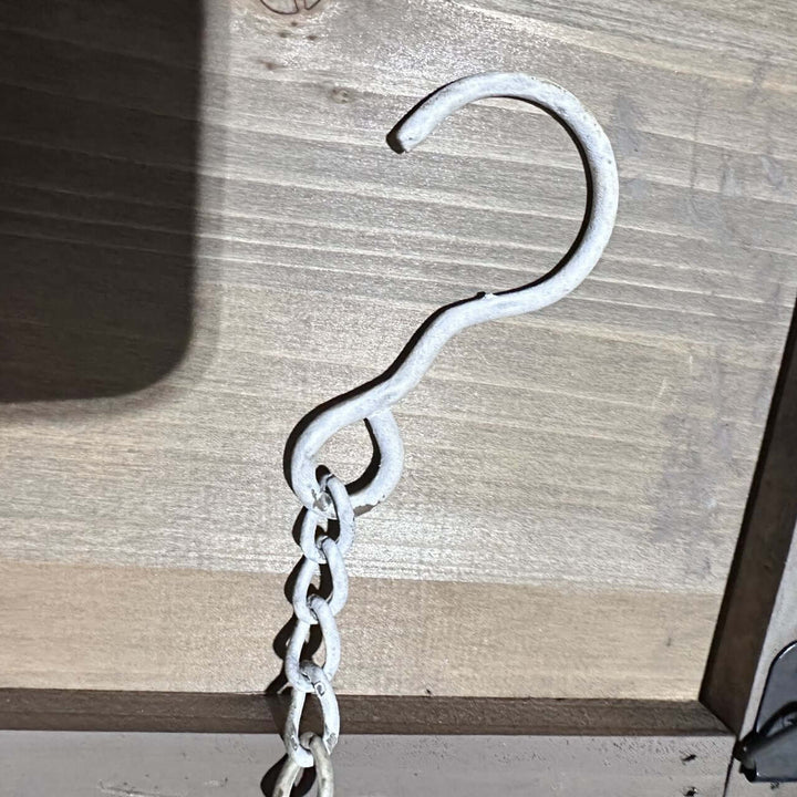 Close-up of a vintage distressed white hook and chain for hanging bird feeder against a wooden backdrop.