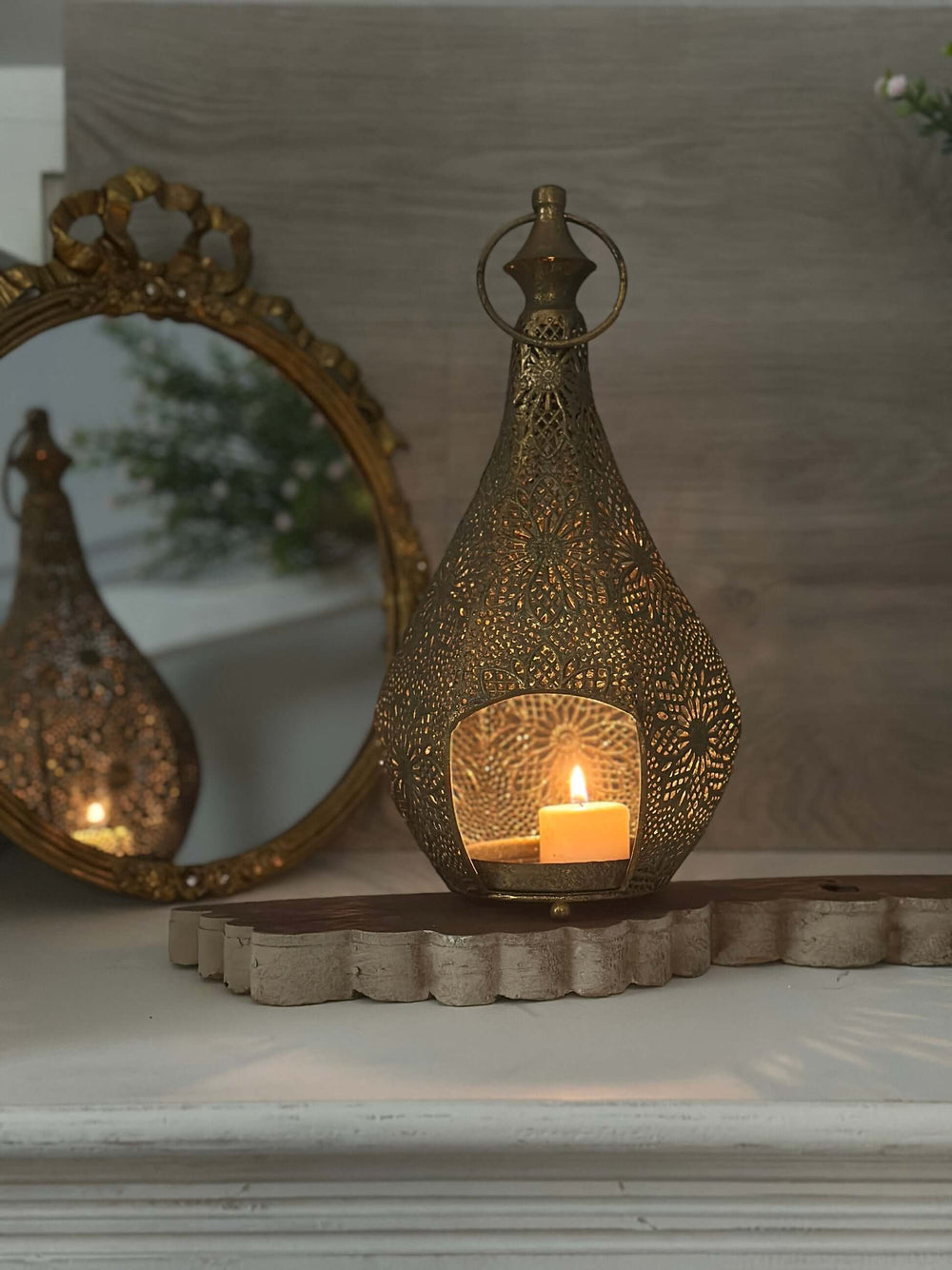 Vintage brass teardrop lantern with floral filigree and glowing candle, reflecting old-world charm and craftsmanship.