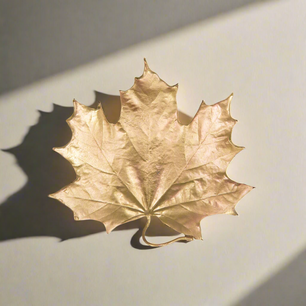 Fall Maple Leaf Trinket Dish in Gold Pewter shaped like a maple leaf with a golden metallic finish, casting a shadow on a light surface.