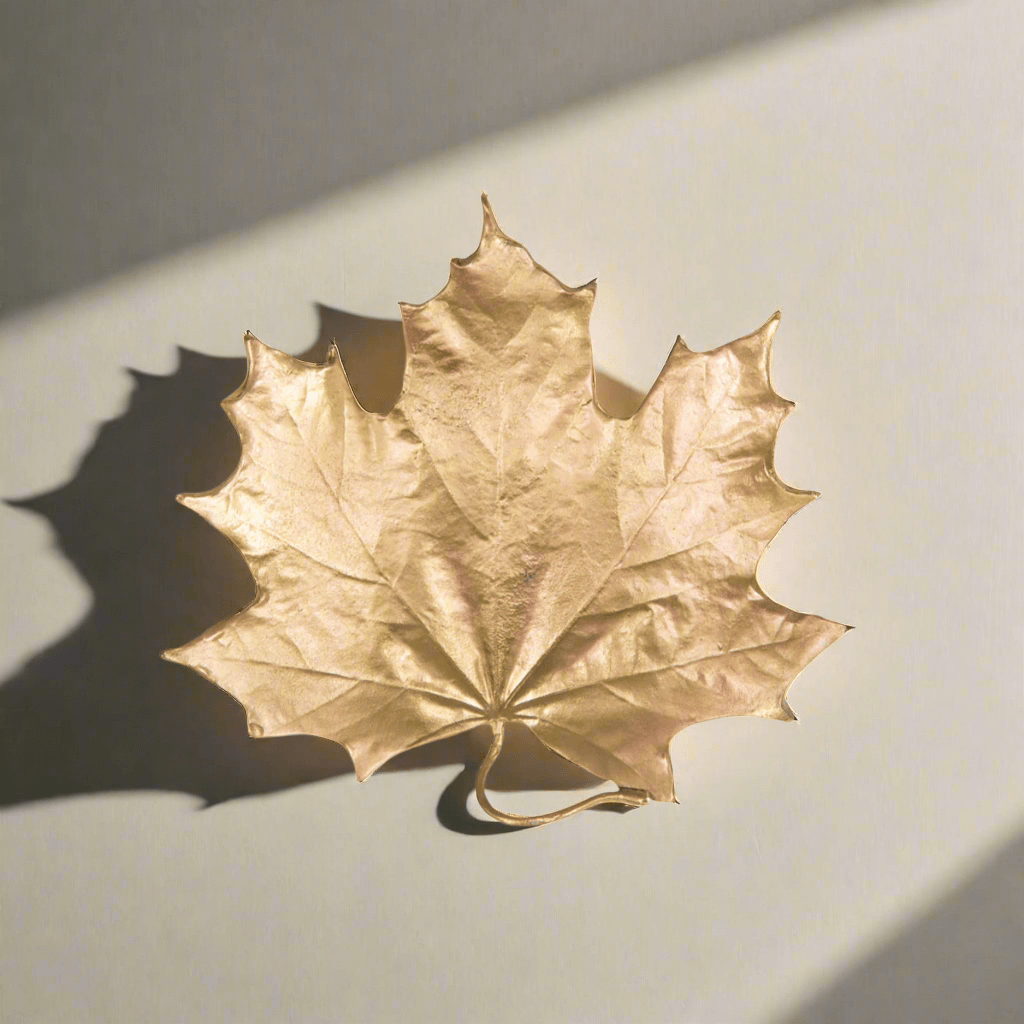 Fall Maple Leaf Trinket Dish in Gold Pewter shaped like a maple leaf with a golden metallic finish, casting a shadow on a light surface.