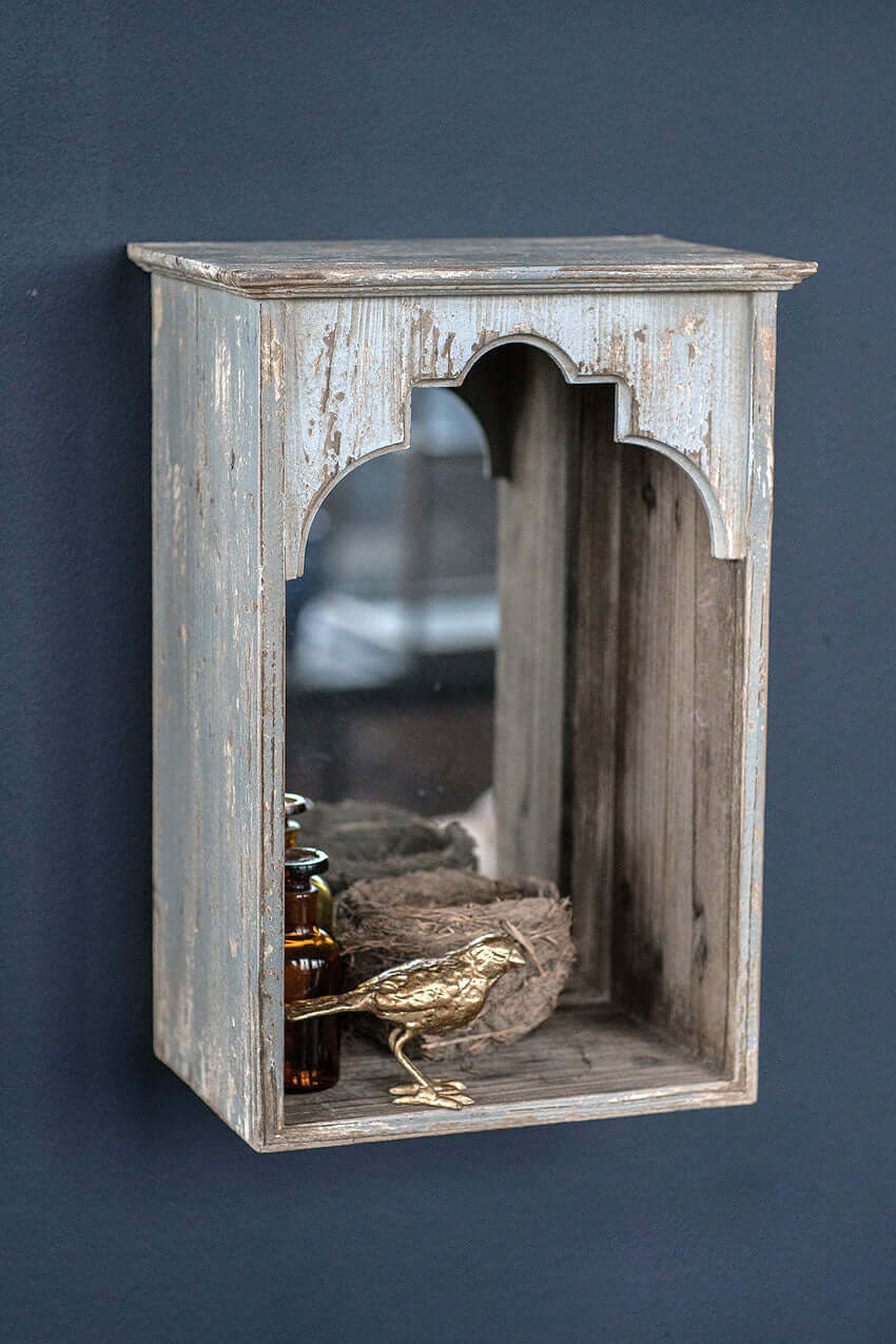 Rustic arched wall niche with mirror and decorative items, enhancing vintage home décor.