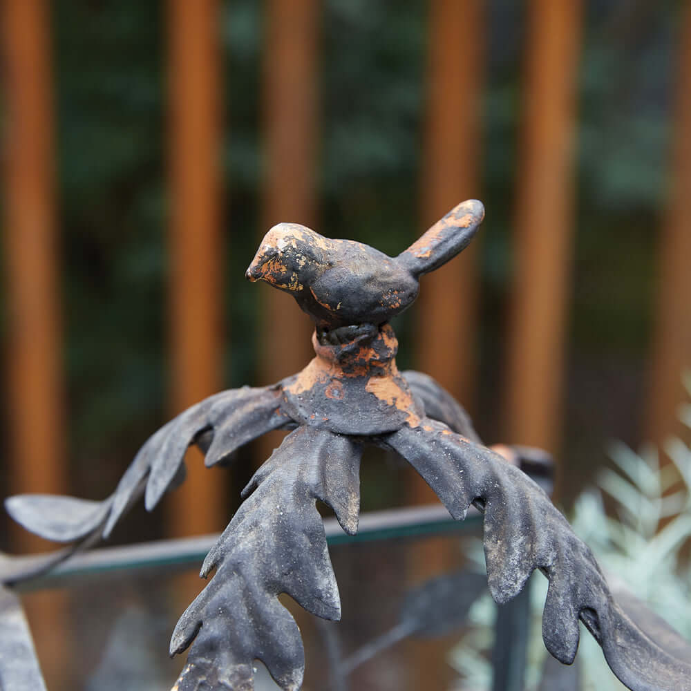 Close-up of a rustic bird figurine atop a lantern with ornamental leaves, perfect for woodland decor.