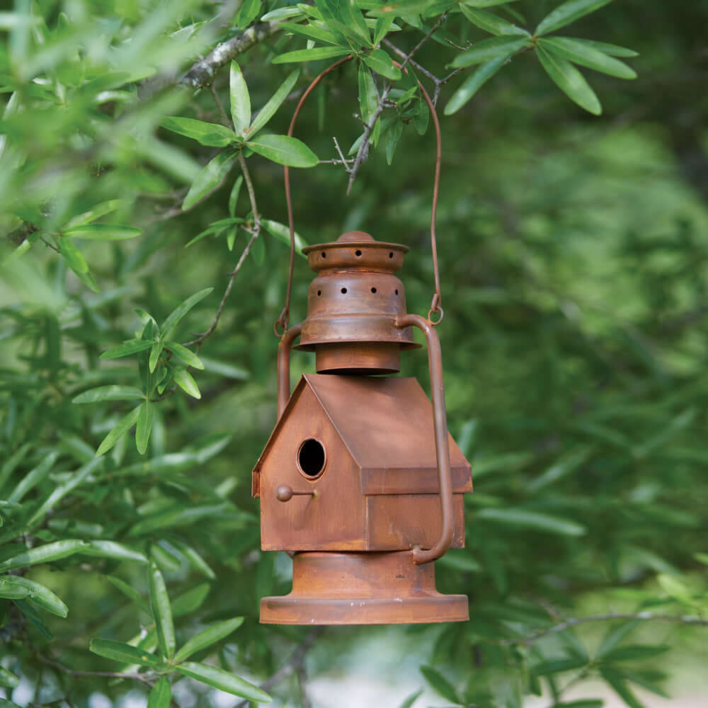 Rustic vintage metal lantern birdhouse hanging among green leaves, combining nostalgia and functionality.