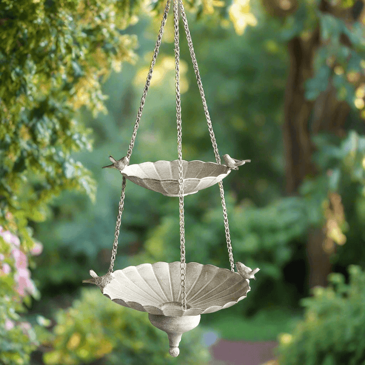 Victorian hanging bird feeder with tiered basins and antique stone finish in a lush garden setting.