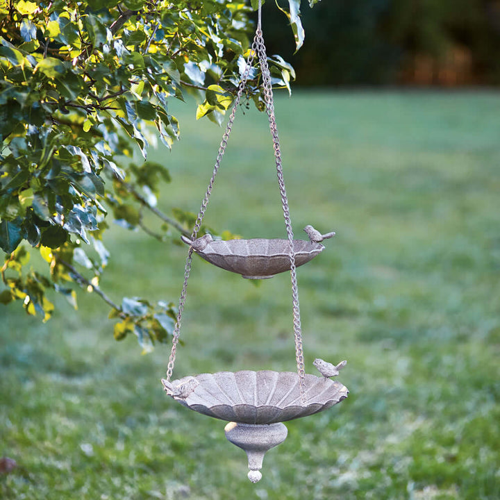 Victorian hanging bird feeder with tiered basins and antique stone finish in a garden setting.