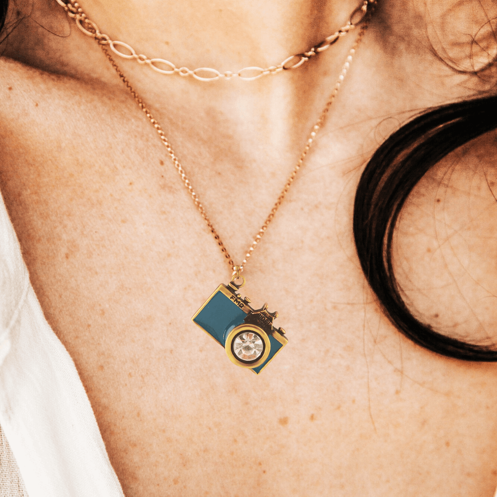 Vintage Camera Pendant Necklace with teal enamel and crystal lens on model's neck, showcasing antique brass finish.
