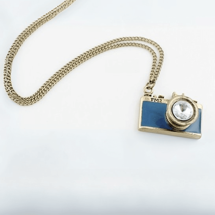 Vintage Camera Pendant Necklace with antique brass finish, teal enamel, and crystal lens on a chain, evoking old-world photography charm.