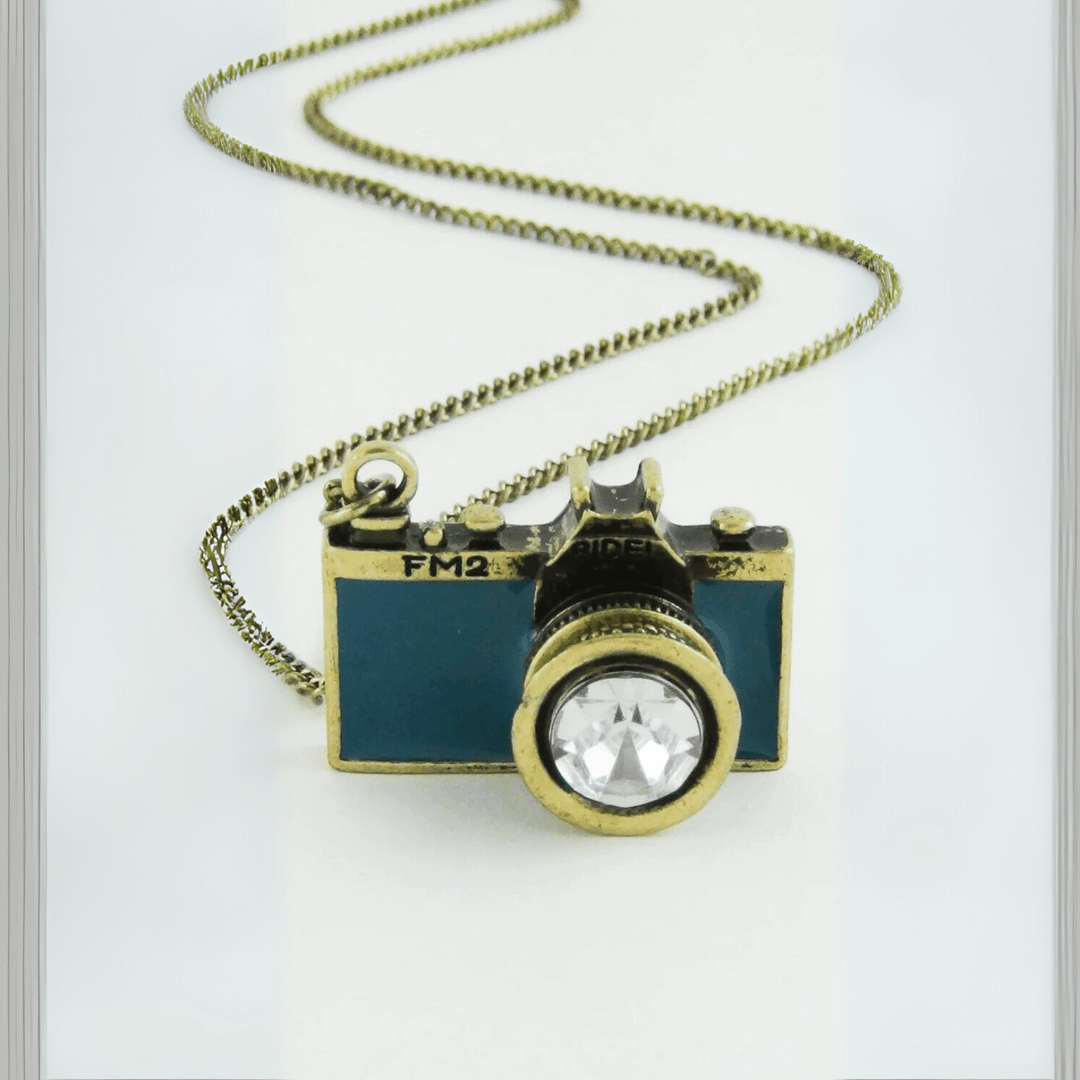 Vintage Camera Pendant Necklace with antique brass finish and teal enamel body, featuring a sparkling crystal lens on a chain