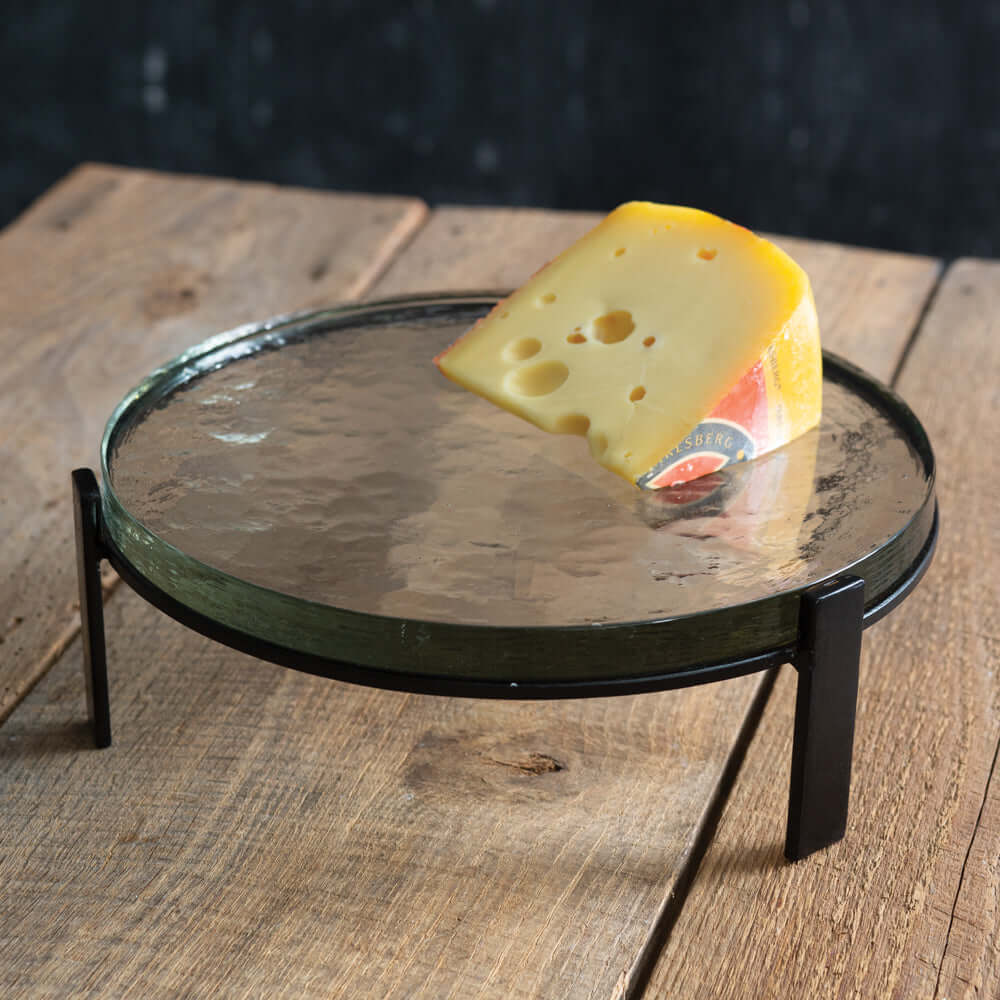 Round glass display stand with a wedge of cheese on a wooden surface