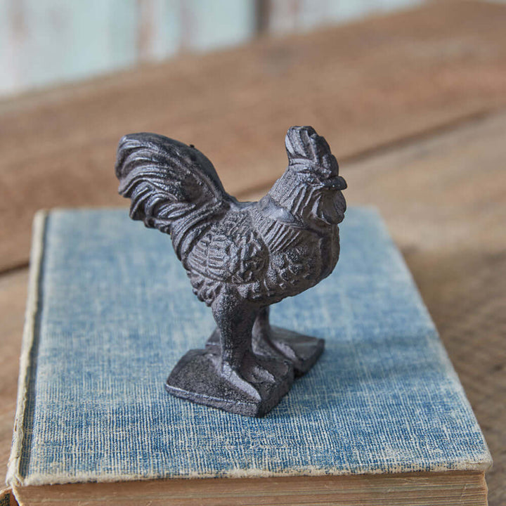 Vintage cast iron rooster paperweight on a blue book, perfect for rustic farmhouse decor.