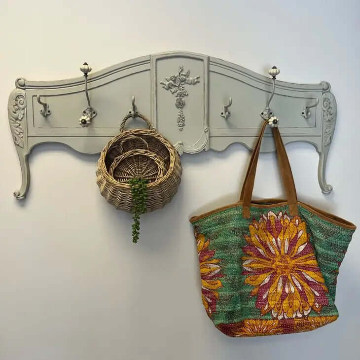 Vintage French country wall-mounted coat rack with floral accents, holding a woven basket and colorful tote bag.