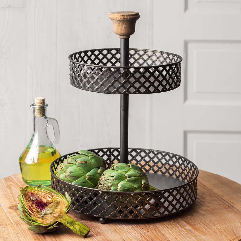 Vintage two-tier fruit basket stand with artichokes and olive oil on a wooden table, showcasing rustic kitchen decor.
