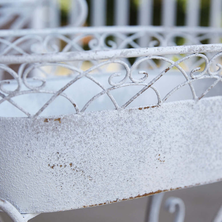 Close-up of vintage white metal planter showcasing intricate scrolled designs and rustic finish.