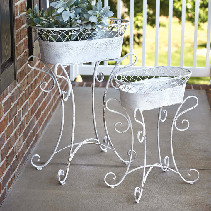 Vintage white metal planters with scrolled stands on a porch, perfect for adding elegance to garden decor.