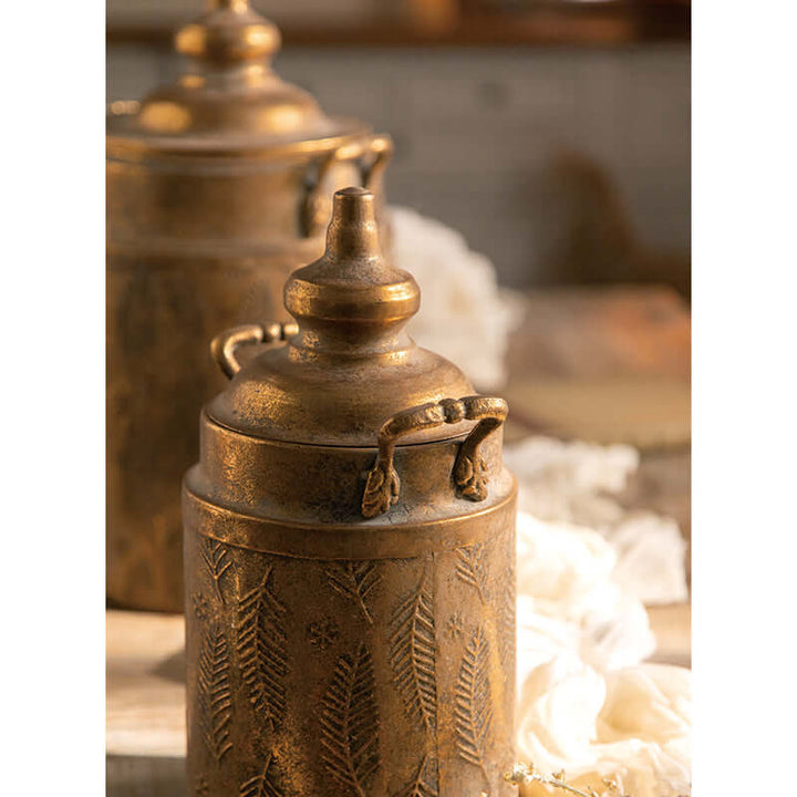 Antique brass embossed storage canisters with lids on a wooden table, evoking a warm farmhouse kitchen atmosphere.