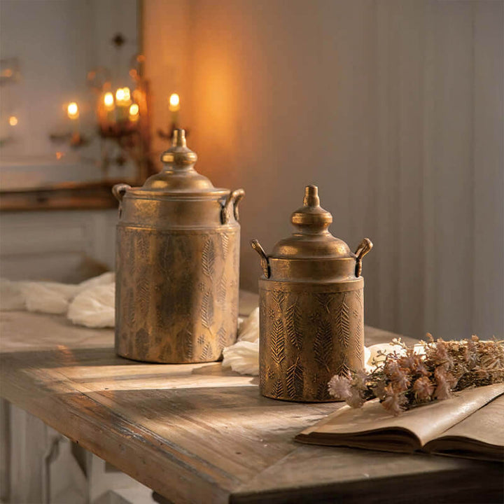 Antique brass embossed storage canisters with lids on a rustic table, exuding vintage farmhouse charm in warm glowing light.