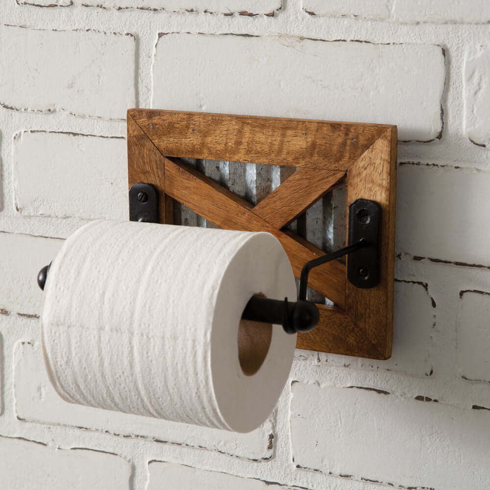 Antique farmhouse toilet paper holder with wooden frame and galvanized metal accent against a brick wall.