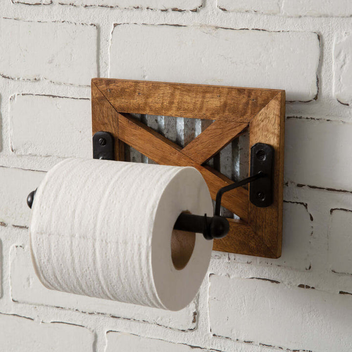Antique farmhouse toilet paper holder with wooden frame and galvanized metal accent against a brick wall.
