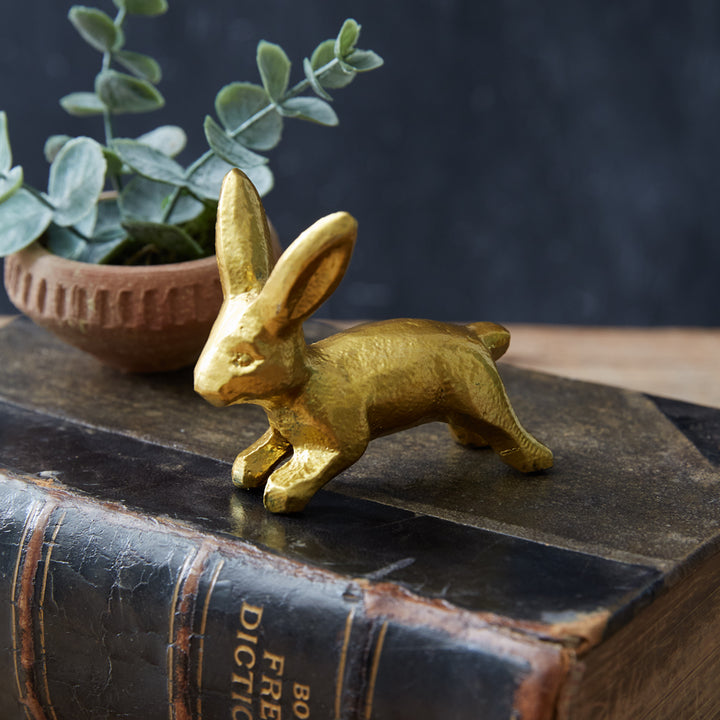 Antique gold bunny figurine on a vintage book with greenery, capturing nostalgic springtime charm.