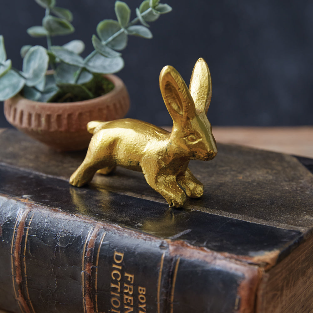 Antique gold bunny figurine on vintage book with plant, evoking springtime nostalgia and vintage décor charm.