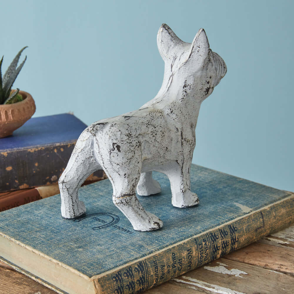 Antique white French Bulldog figurine with vintage weathered finish on a stack of old books.