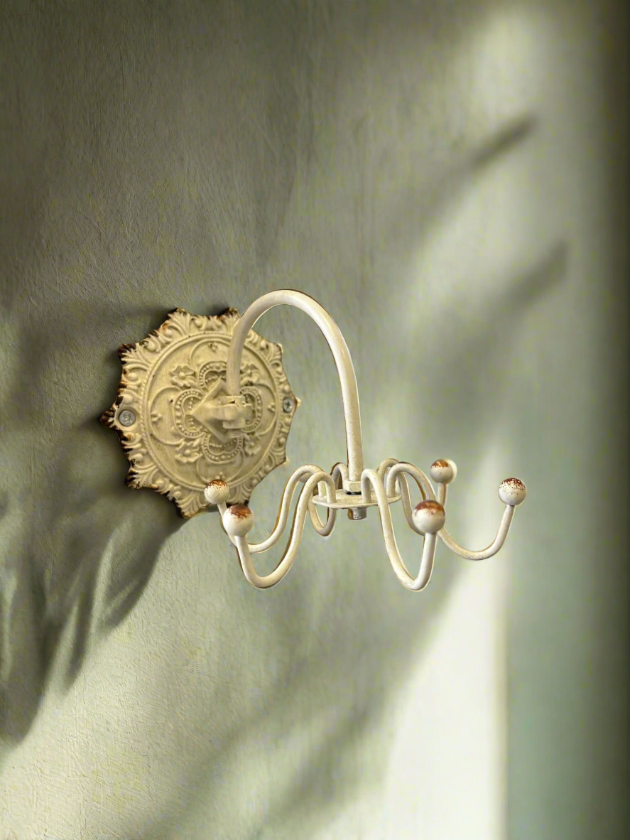 Antique white wall hook with ornate medallion backplate, featuring elegant curves and vintage charm.
