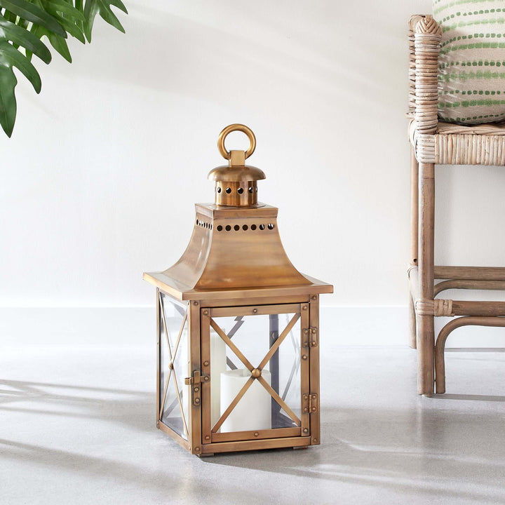 Antique brass lantern with crossbar glass and hanging ring, exuding vintage charm and warm elegance on a sunlit floor.