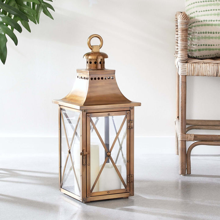 Antique brass lantern with crossbar glass, hanging ring, and aged finish, evoking vintage charm in a serene home setting.