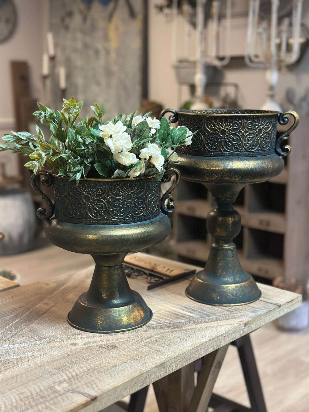 Antique bronze ornate metal urns with floral design on wooden table; home decor reflecting old-world elegance.