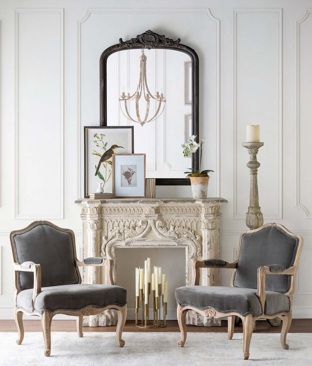 Antique white fireplace mantel with distressed vintage finish, elegant chairs, and decorative mirror in a classic room setup.