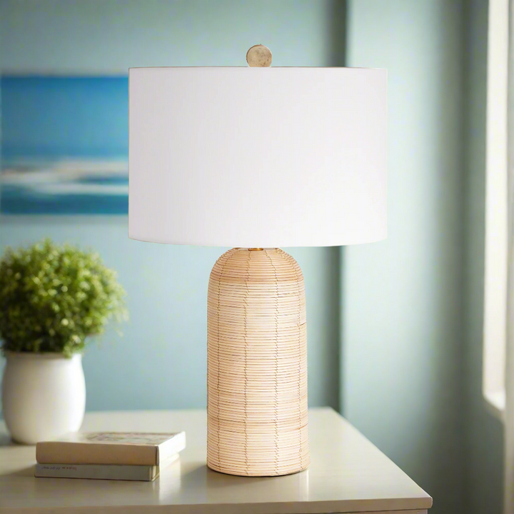 Coastal woven rattan table lamp with white drum shade on a side table, evoking summer mornings and seaside elegance.
