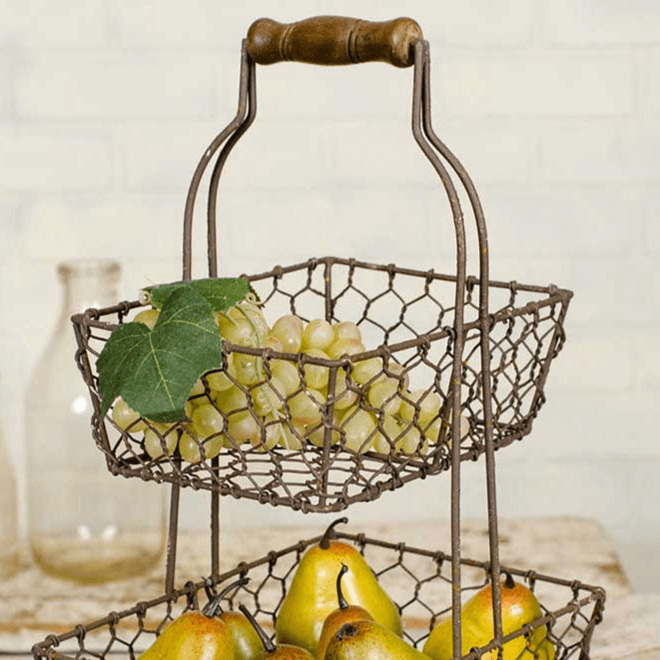 Farmhouse two-tier fruit basket with chicken wire design, holding grapes and pears, featuring a wooden handle and rustic metal finish.