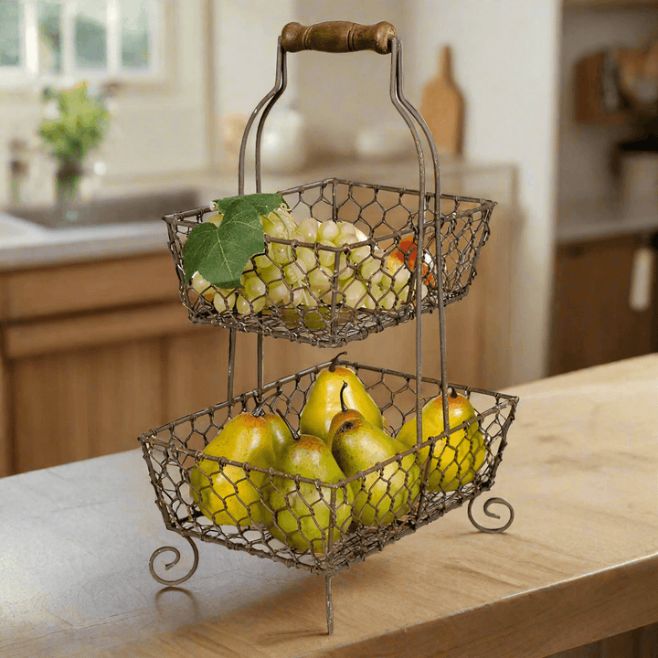 Farmhouse chicken wire two-tier fruit basket with grapes and pears on kitchen counter, featuring vintage design with wooden handle.