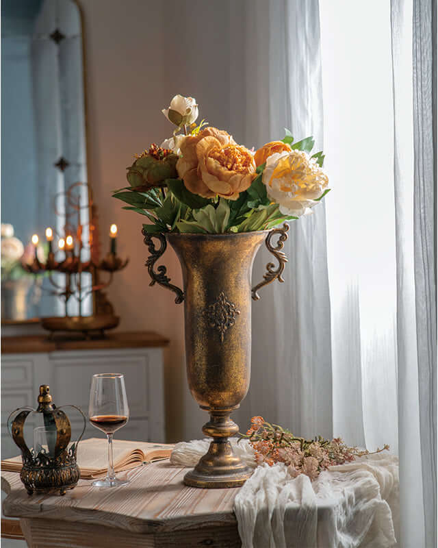 Antique gold urn vase with flowers in French country decor setting, featuring ornate handles and embossed medallion.