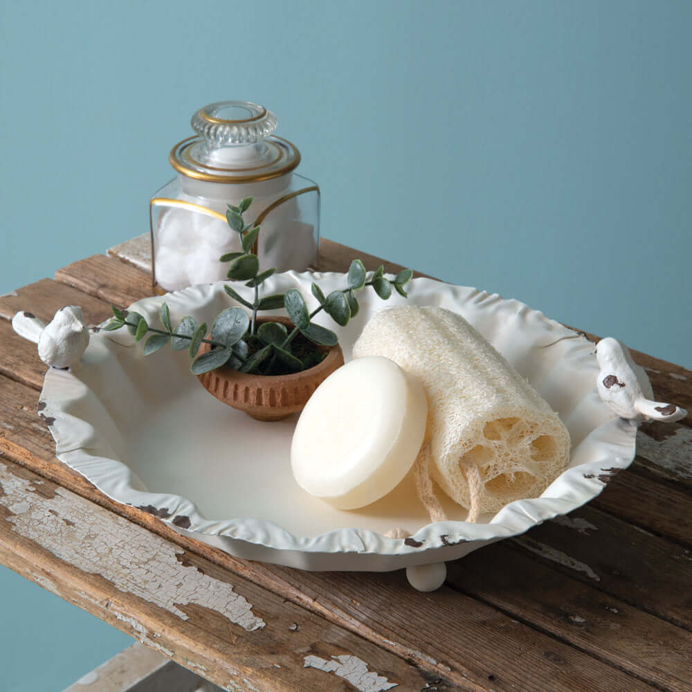 French country decorative bird dish with soap, loofah, and greenery on rustic wood.