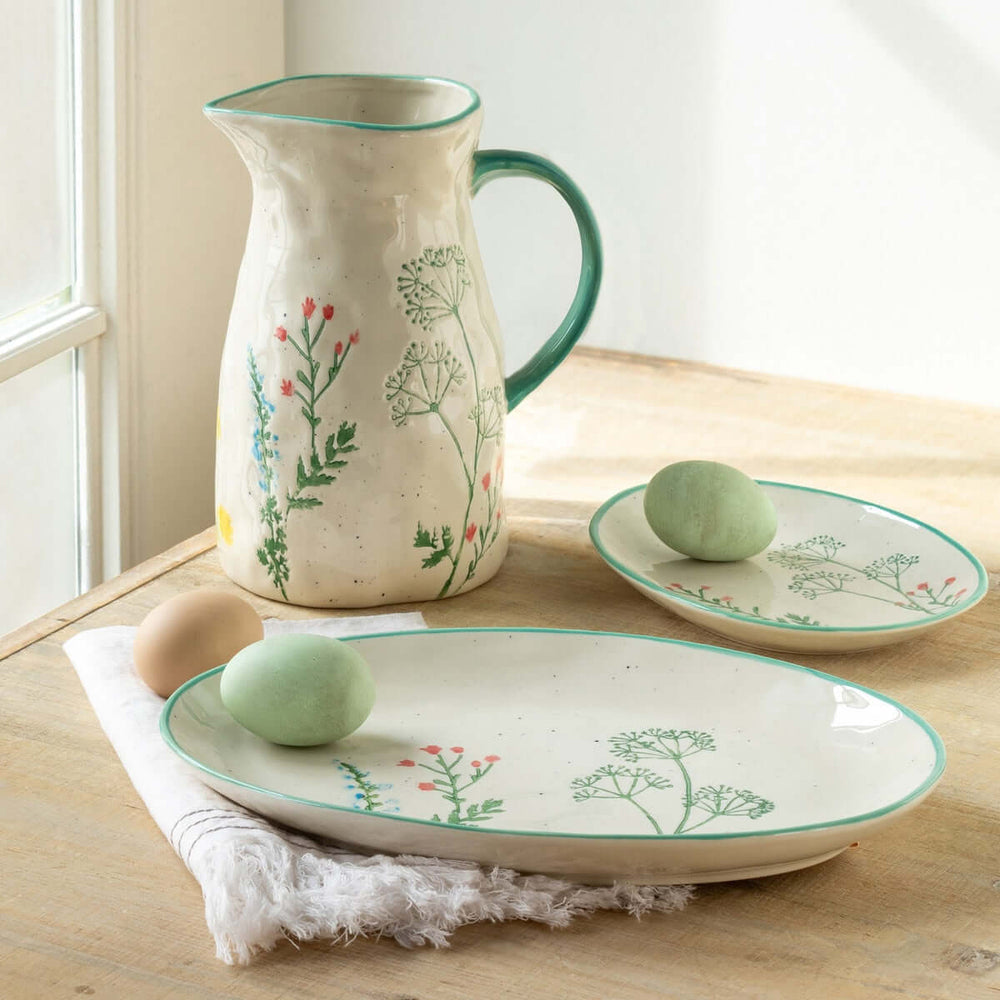 Hand-Painted Ceramic Wildflower Pitcher with floral motifs, accompanied by matching plates, on a rustic wooden table.